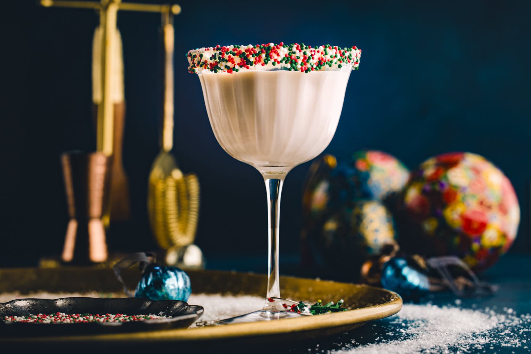 A glass of Sugar Cookie Martini (with holiday sprinkles on the rim) - on a festive tray.