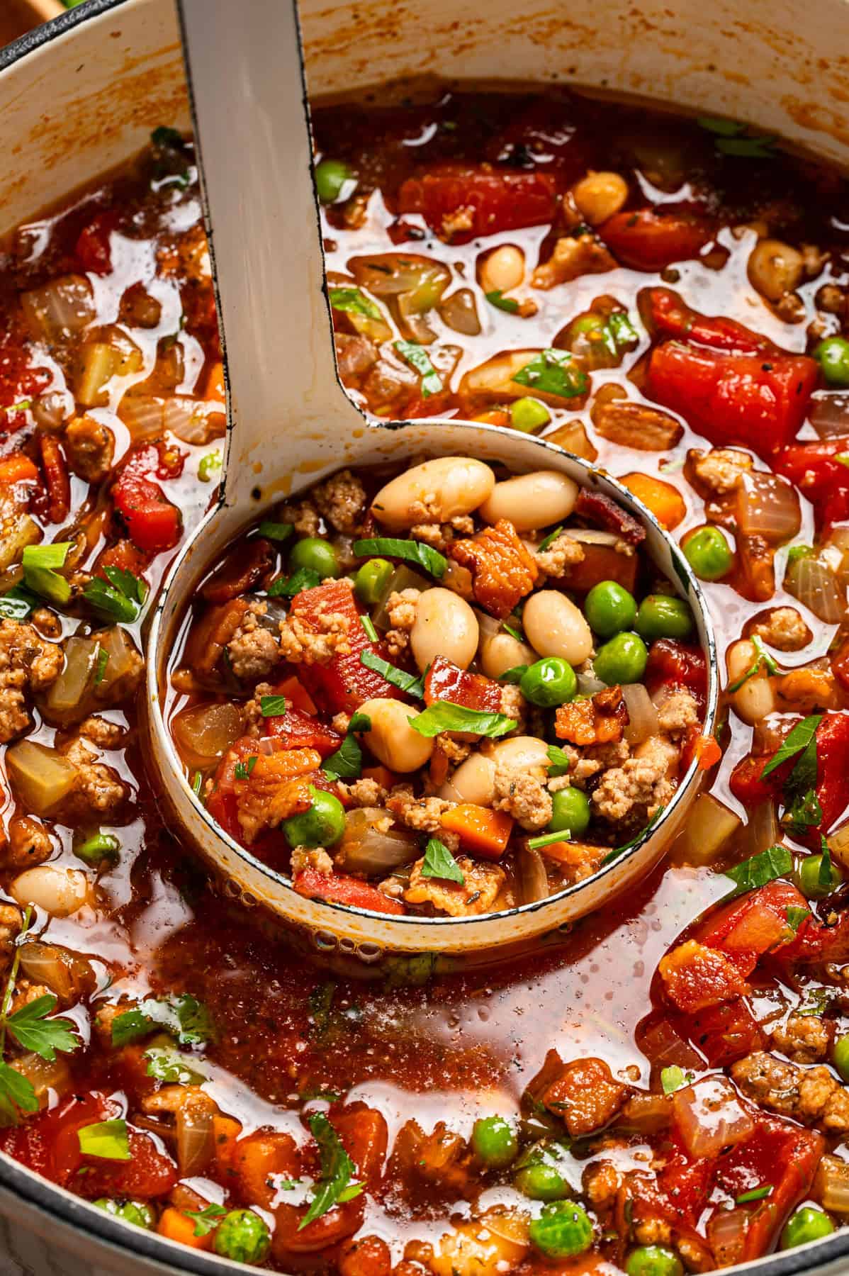 Ground Turkey Soup with Carrots, Peas, Beans, Bacon, Tomatoes, Herbs - in a Dutch oven with a ladle.