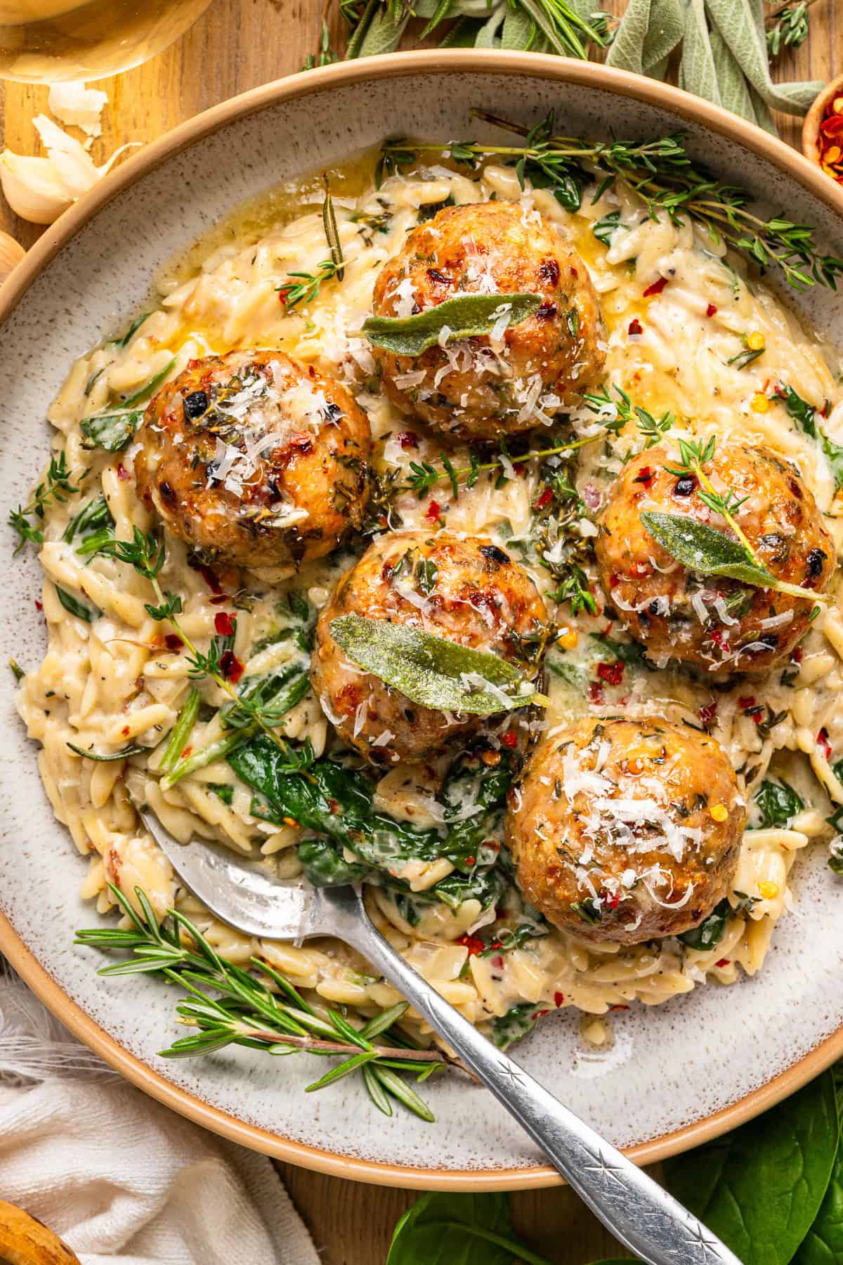 Oven-Baked Chicken Meatballs with Creamy Parmesan Spinach Orzo - on a plate topped with fresh herbs.