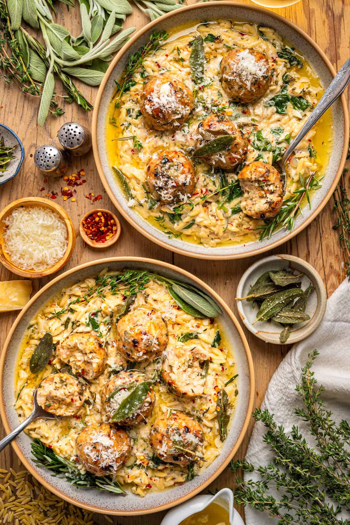 Overhead view of two plates of Oven-Baked Chicken Meatballs with Creamy Parmesan Spinach Orzo topped with herbs.