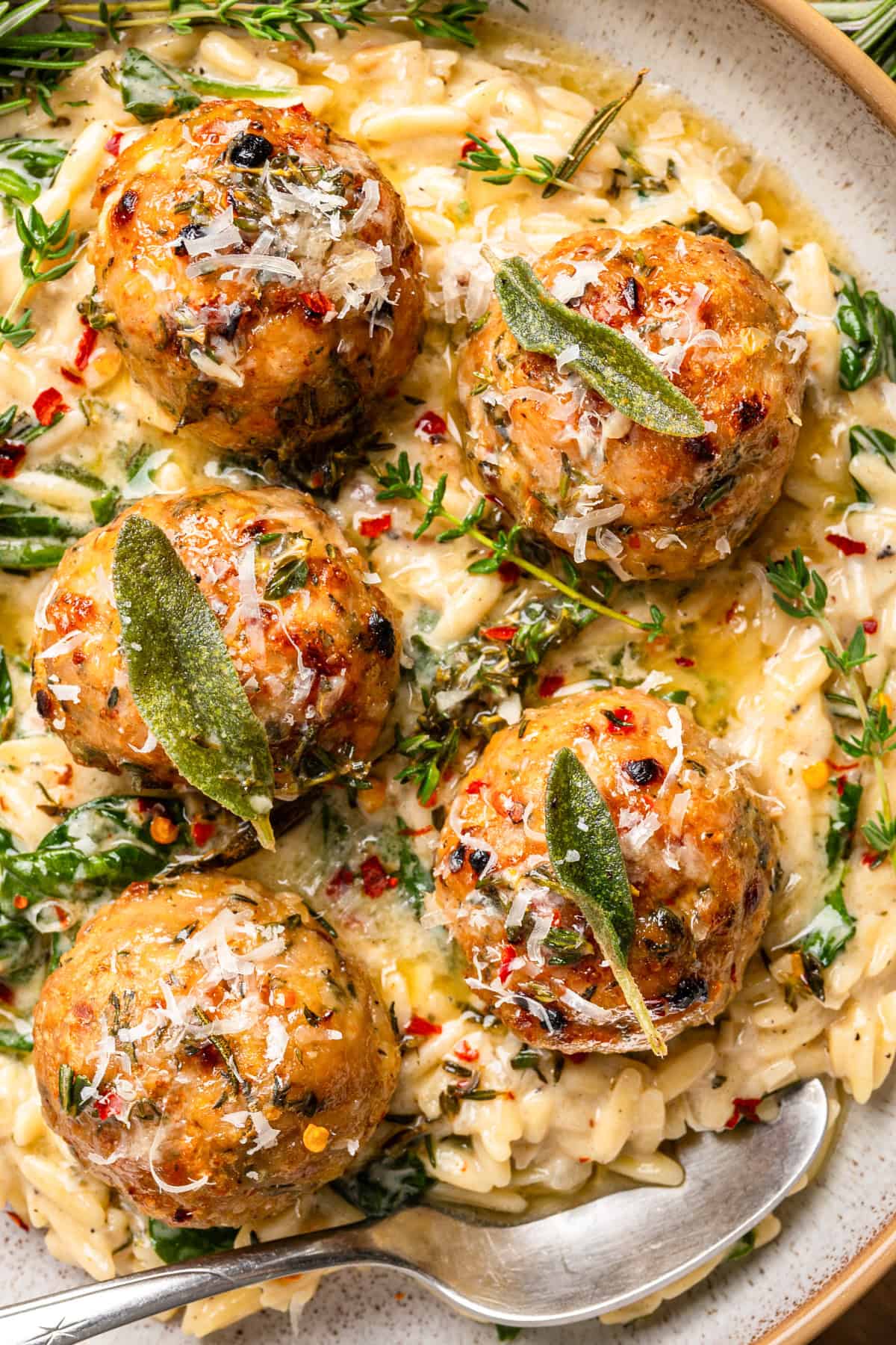 Oven-Baked Chicken Meatballs with Creamy Parmesan Spinach Orzo topped with fresh herbs - on a plate.