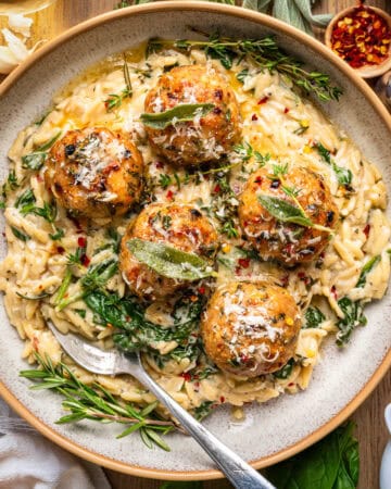Oven-Baked Chicken Meatballs with Creamy Parmesan Spinach Orzo topped with herbs - on a plate.
