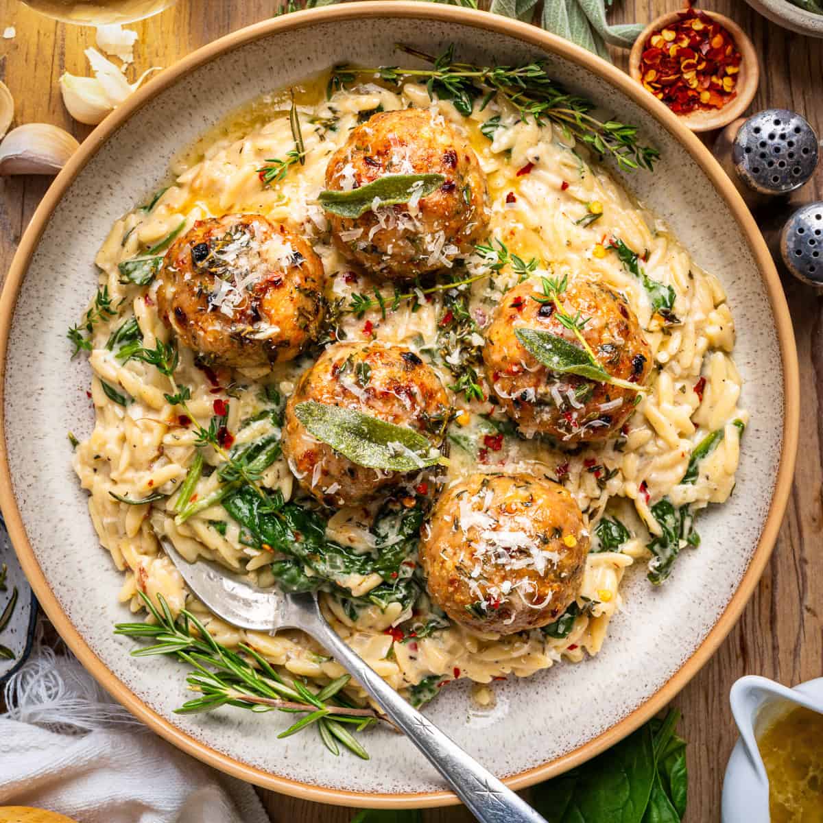 Oven-Baked Chicken Meatballs with Creamy Parmesan Spinach Orzo topped with herbs - on a plate.