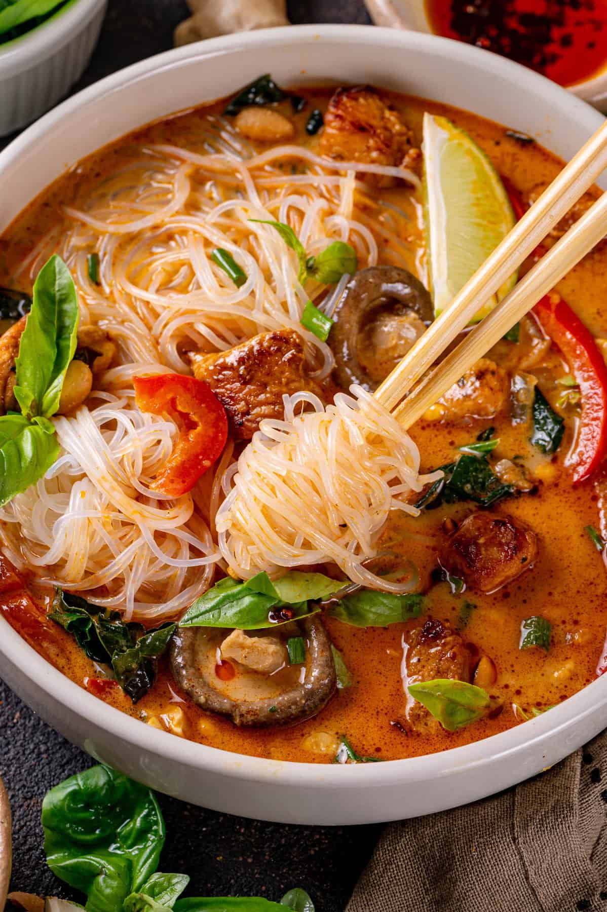 Thai chicken curry soup (with noodles, red bell peppers, and mushrooms) - in a bowl, with noodles wrapped around chopsticks. 