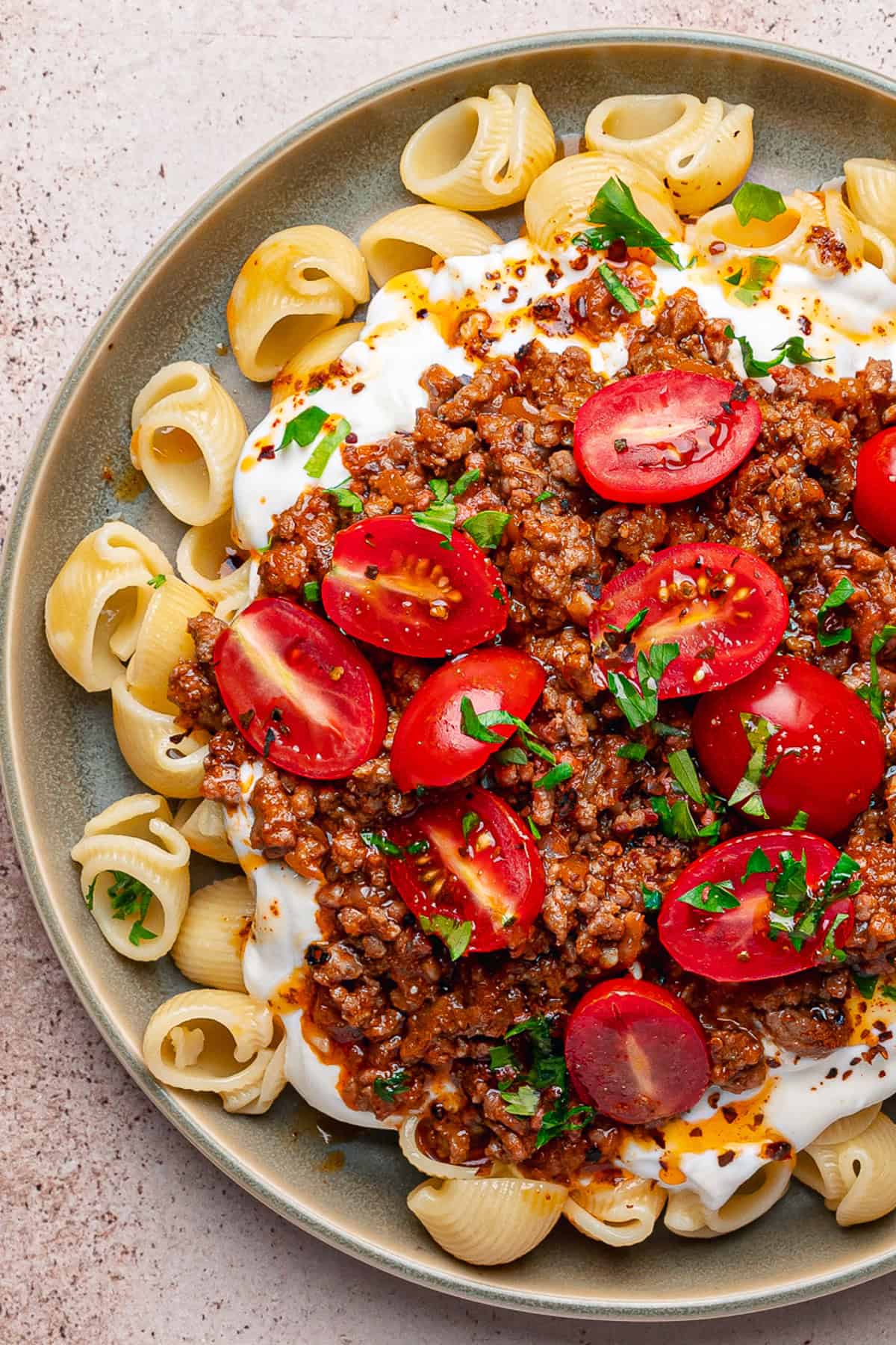 Turkish Pasta A plate of Turkish pasta shells topped with creamy yogurt sauce, seasoned ground meat, halved cherry tomatoes, chopped parsley, and a sprinkle of red pepper flakes.
