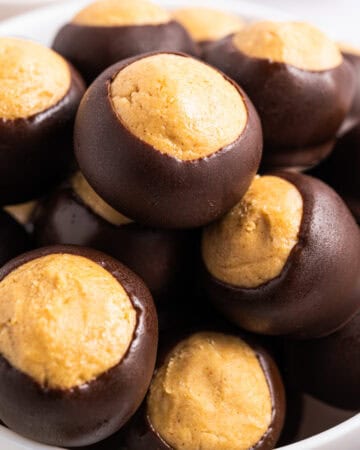 A bowl filled with buckeye candy, featuring creamy peanut butter centers partially dipped in smooth dark chocolate, leaving the tops exposed.