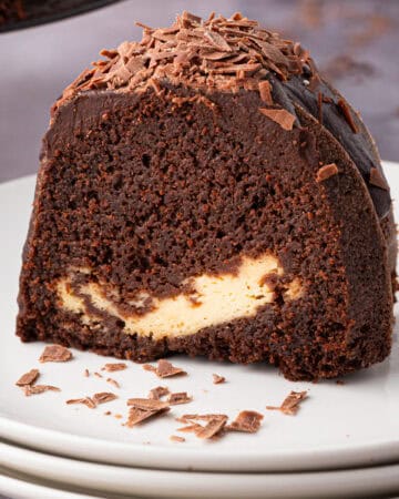 A slice of Guinness chocolate bundt cake with a creamy filling and chocolate shavings on top, served on a white plate.