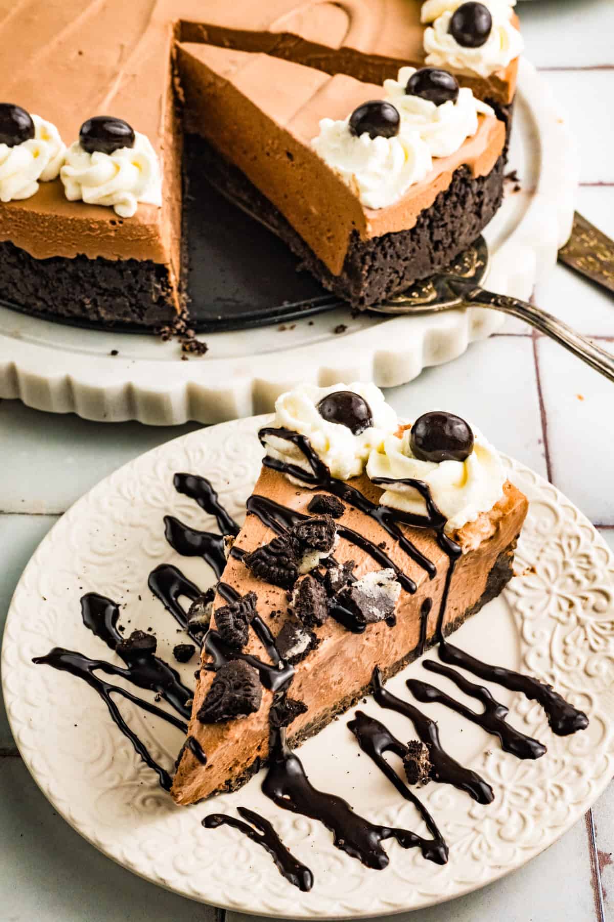 Mudslide Pie A slice of Mudslide Pie with an Oreo crust is served on a plate, topped with whipped cream and chocolate pieces, and drizzled with chocolate sauce. The rest of the pie is in the background.