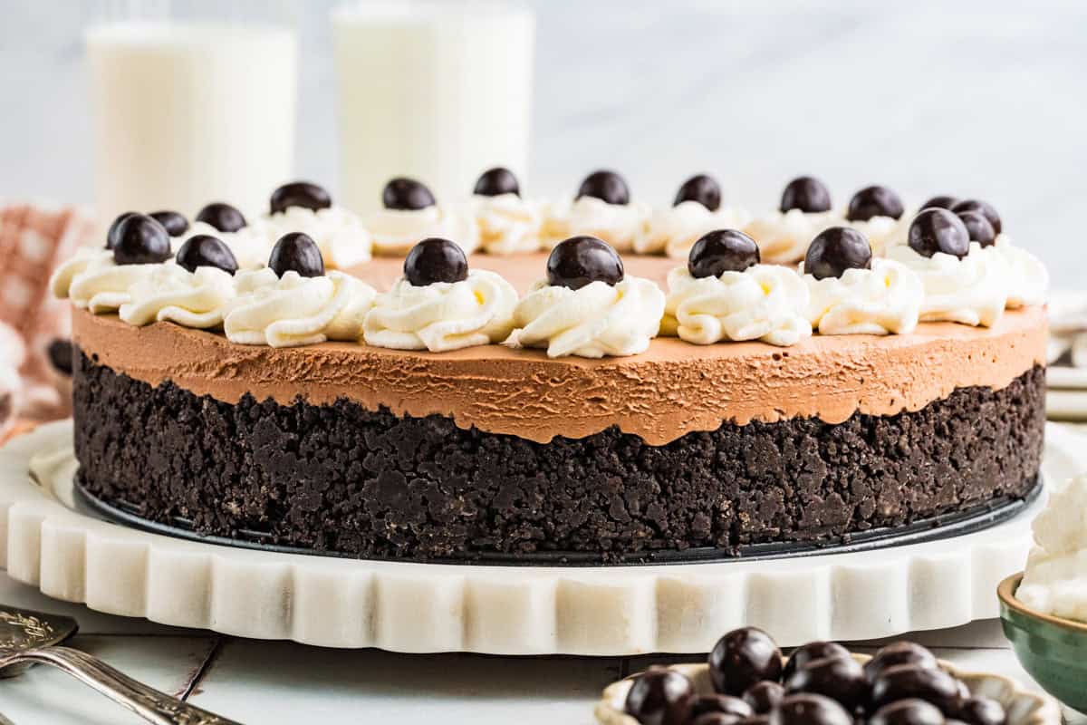 Mudslide Pie A chocolate Mudslide Pie with a dark cookie crust, topped with swirls of whipped cream and chocolate-covered espresso beans, sits on a white marble platter. Two glasses of milk are in the background.
