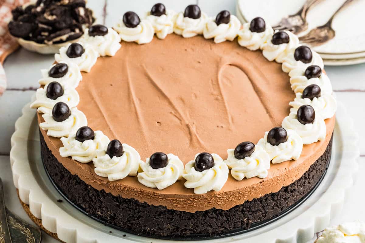 Mudslide Pie A chocolate Mudslide Pie with an Oreo cookie crust, topped with whipped cream swirls and chocolate-covered coffee beans arranged in a circle on a white plate.