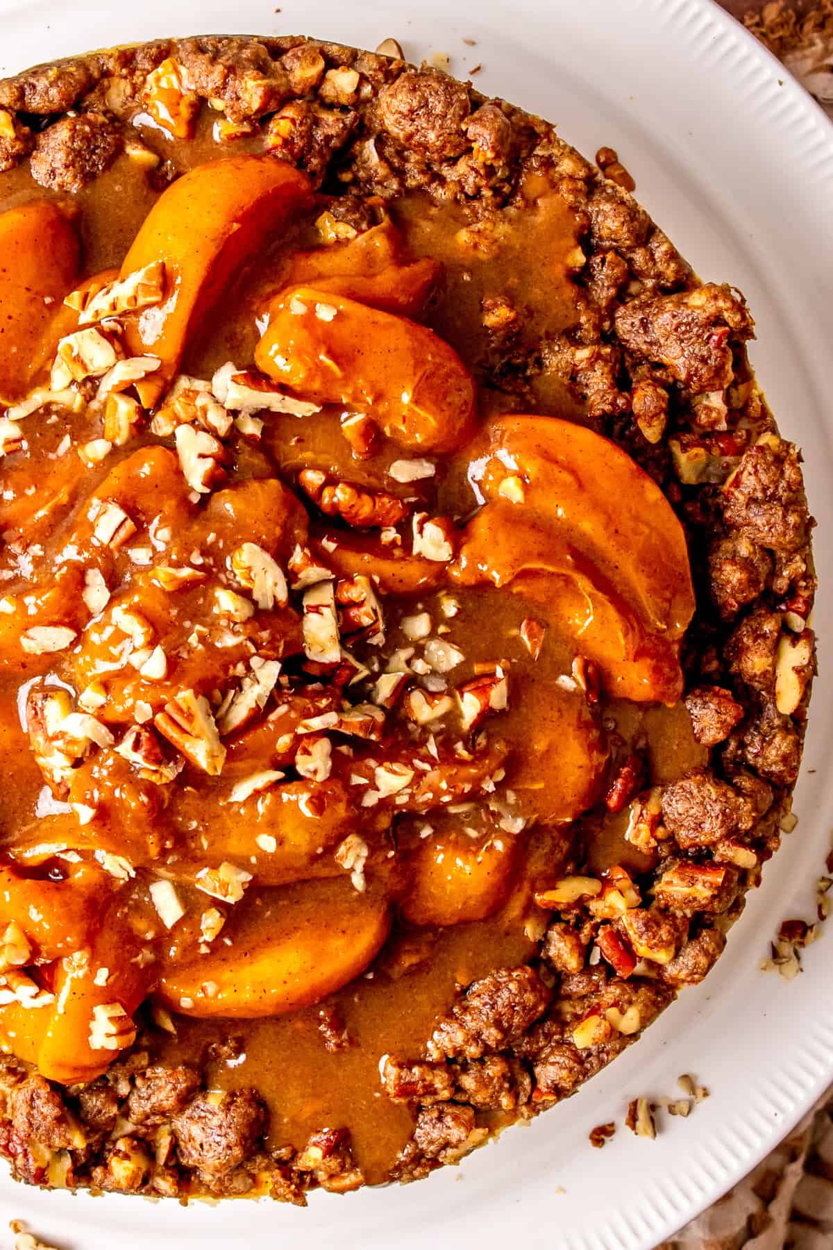 A close-up of Peach Cobbler Cheesecake, topped with cooked peaches, streusel topping, and chopped pecans on a white plate.