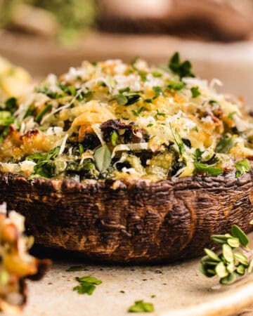 A close-up of a large portobello mushroom cap, stuffed with a golden, cheesy herb-and-spinach filling and garnished with fresh, chopped herbs, served on a rustic plate.