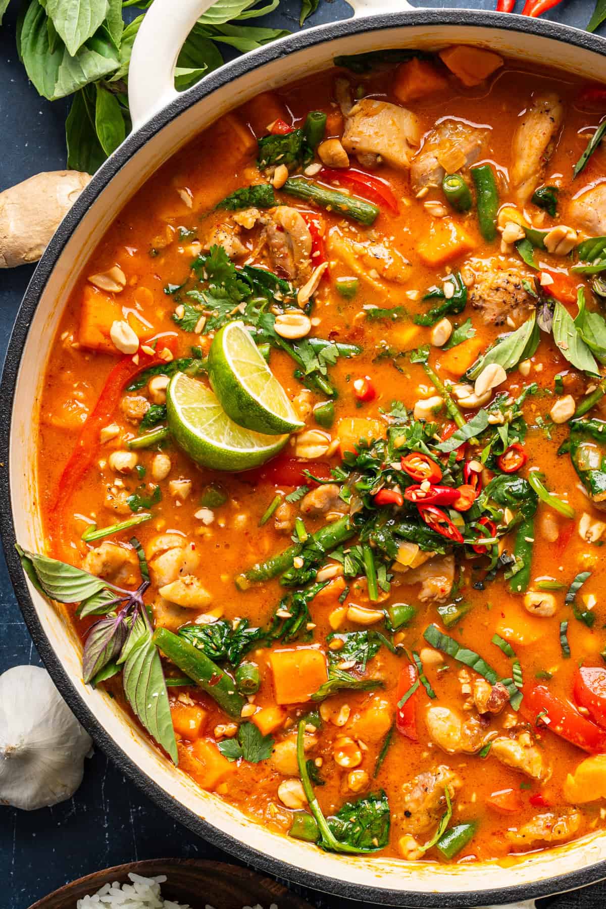 Thai Chicken Curry A pot of vibrant Thai curry with chicken, sweet potatoes, green beans, red bell peppers, and topped with lime wedges, fresh herbs, chopped peanuts, and sliced chili peppers.