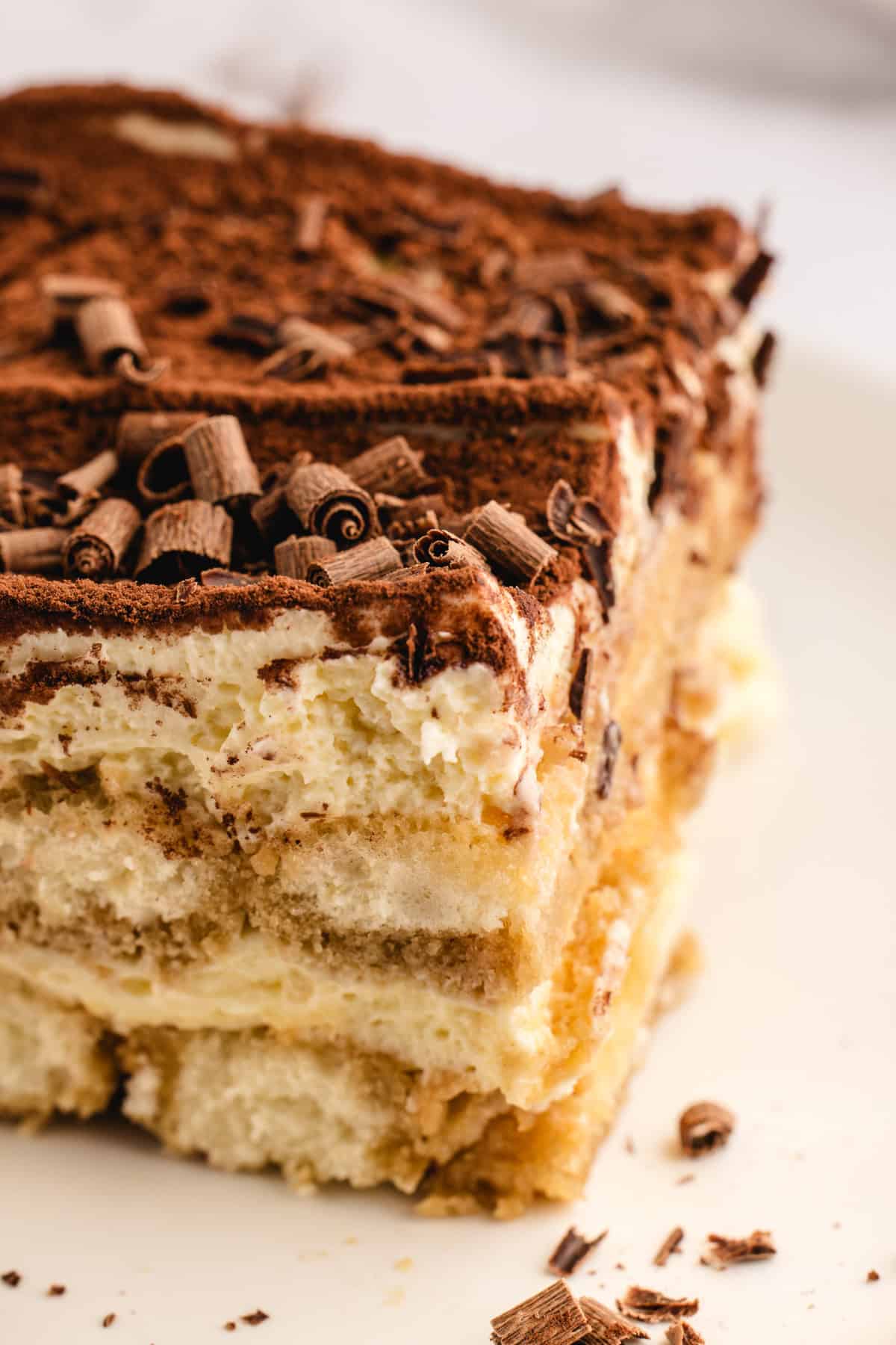 Classic Italian Tiramisu A close-up of a slice of classic tiramisu on a white plate, showing layers of coffee-soaked ladyfingers, creamy mascarpone, and a dusting of cocoa powder, topped with chocolate shavings.