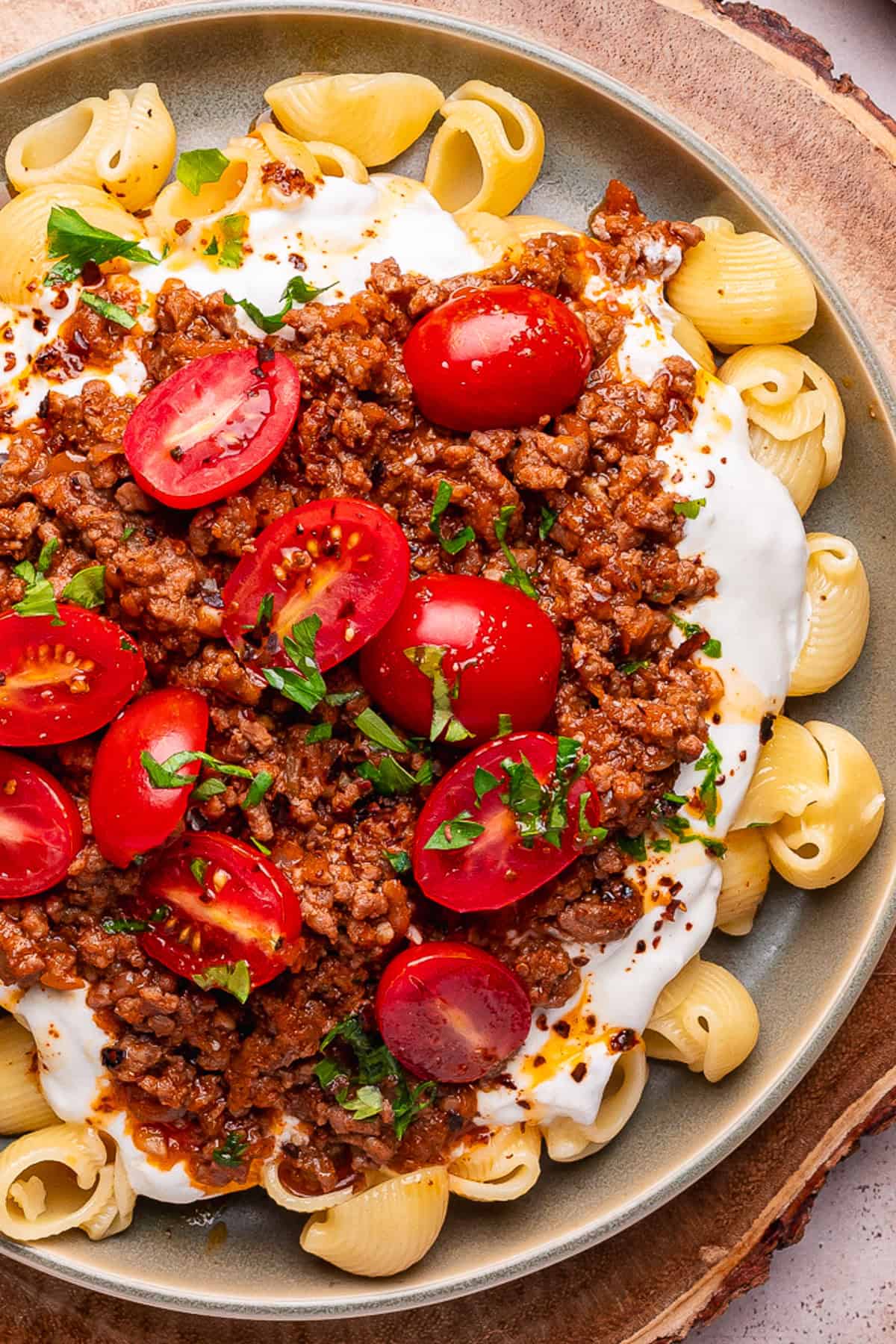 Turkish Pasta A plate of Turkish pasta shells topped with creamy white sauce, seasoned ground meat, halved cherry tomatoes, and chopped fresh herbs, served on a ceramic dish.