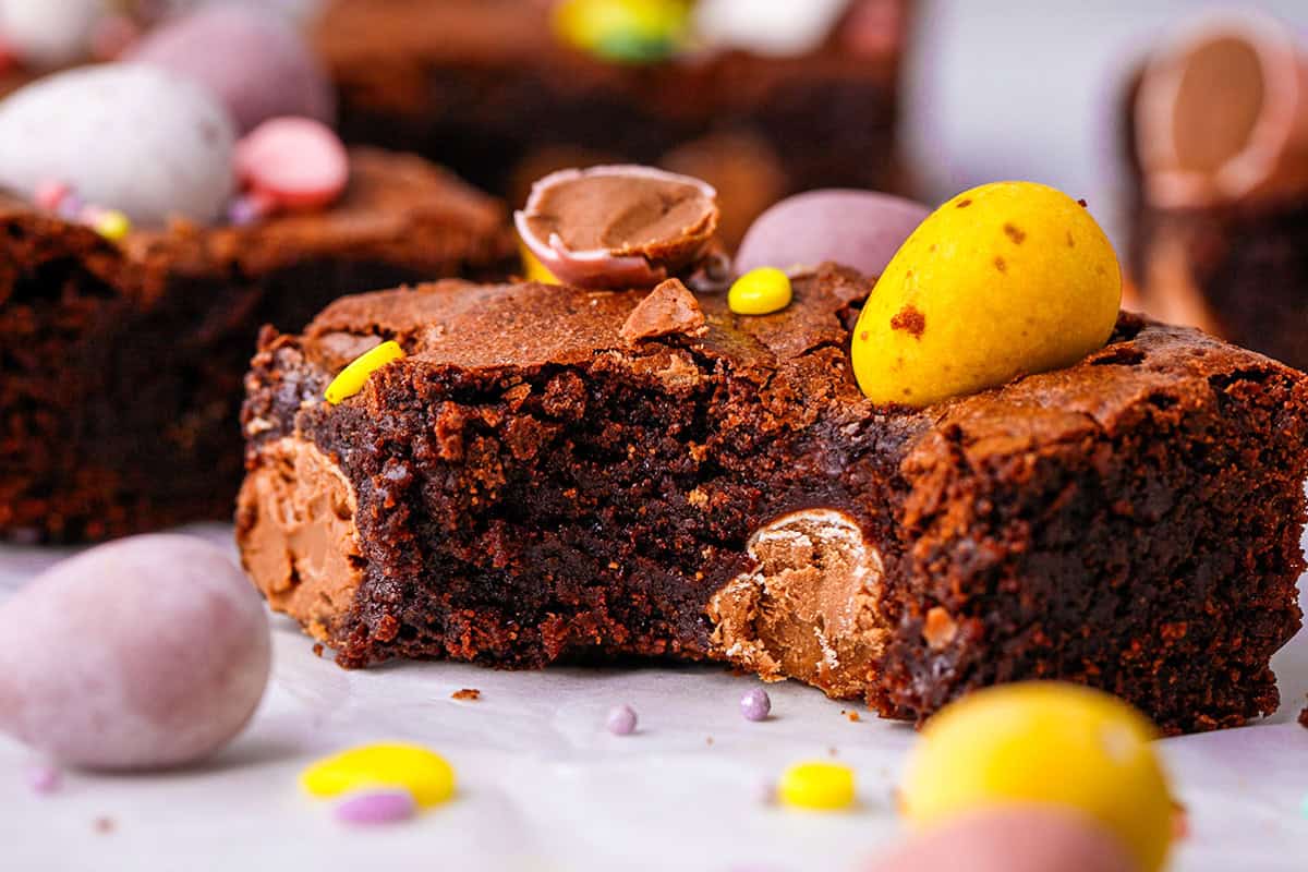 A rich, fudgy brownie topped with colorful candy-coated chocolate eggs, with more chocolate eggs scattered around.