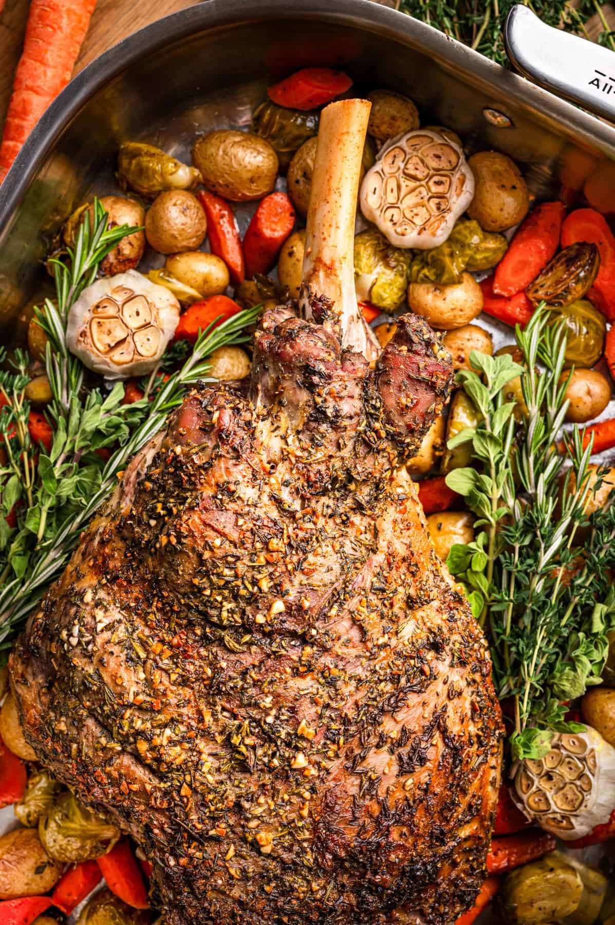 Best Easter Side Dishes for Easter Lamb Herb-crusted roasted leg of lamb in a pan surrounded by roasted potatoes, carrots, halved garlic bulbs, fresh rosemary, and oregano.