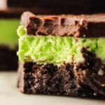 A close-up of a mint chocolate brownie with layers of dark chocolate, green mint filling, and a fudgy brownie base, showing a creamy texture and a bite taken out of the top.