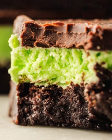 A close-up of a mint chocolate brownie with layers of dark chocolate, green mint filling, and a fudgy brownie base, showing a creamy texture and a bite taken out of the top.