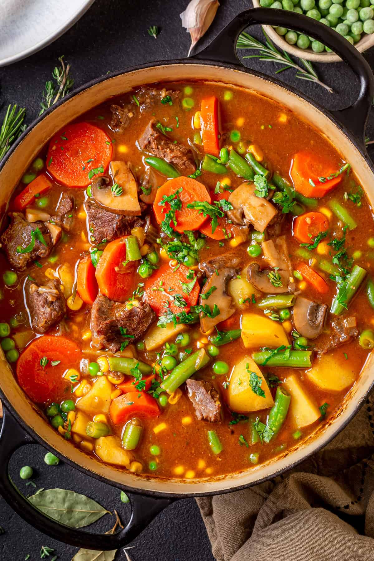 Mulligan Stew (Hobo Stew) A pot of hearty mulligan stew filled with chunks of beef, carrots, potatoes, green beans, peas, mushrooms, and a rich reddish broth, garnished with fresh herbs.