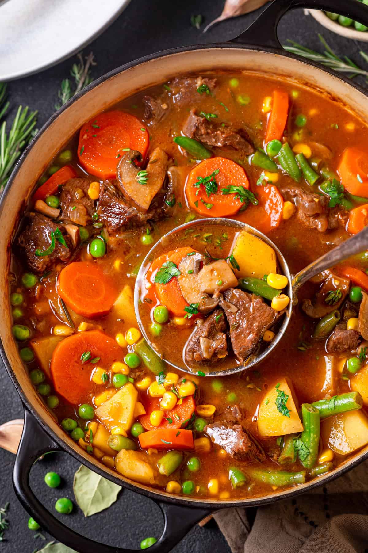 Mulligan Stew, also known as Hobo Stew, is a classic one-pot beef-and-vegetable soup featuring tender beef, potatoes, carrots, corn, peas, and a rich, savory beef broth. A pot of hearty mulligan stew with chunks of beef, carrots, potatoes, green beans, peas, and corn in a rich broth, with a ladle lifting a serving from the pot. Fresh herbs are sprinkled on top.