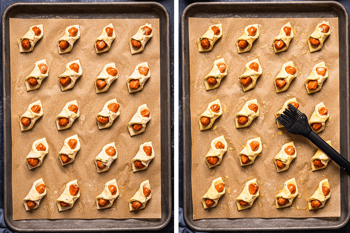 Two baking sheets lined with parchment paper, each holding rows of unbaked pastry rolls filled with small sausages; a pastry brush is being used to brush egg wash on some unbaked pigs in a blanket on the right sheet.