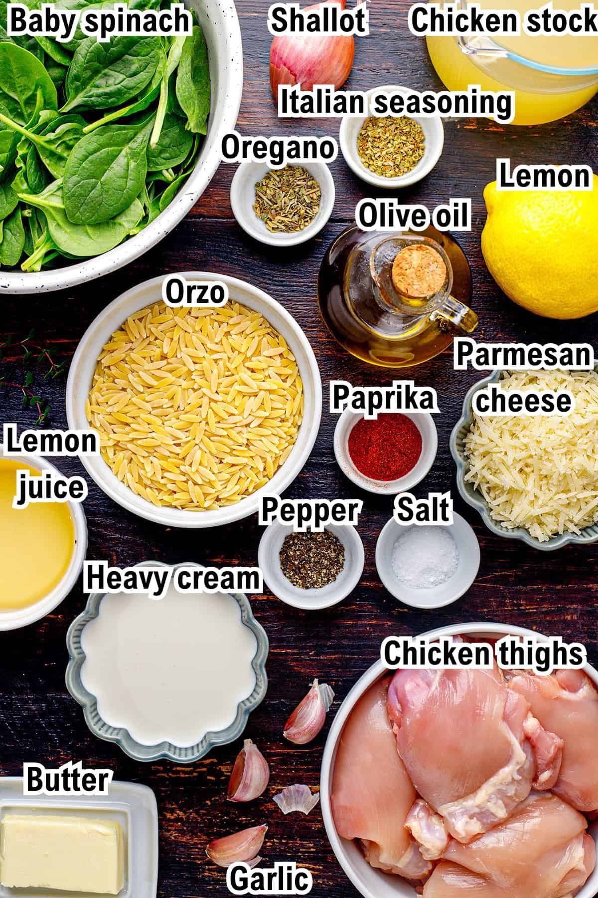 A flat lay of ingredients for a Lemon Chicken Orzo recipe, including baby spinach, orzo, chicken thighs, heavy cream, parmesan cheese, lemon, lemon juice, shallot, garlic, butter, olive oil, Italian seasoning, oregano, paprika, salt, and pepper.