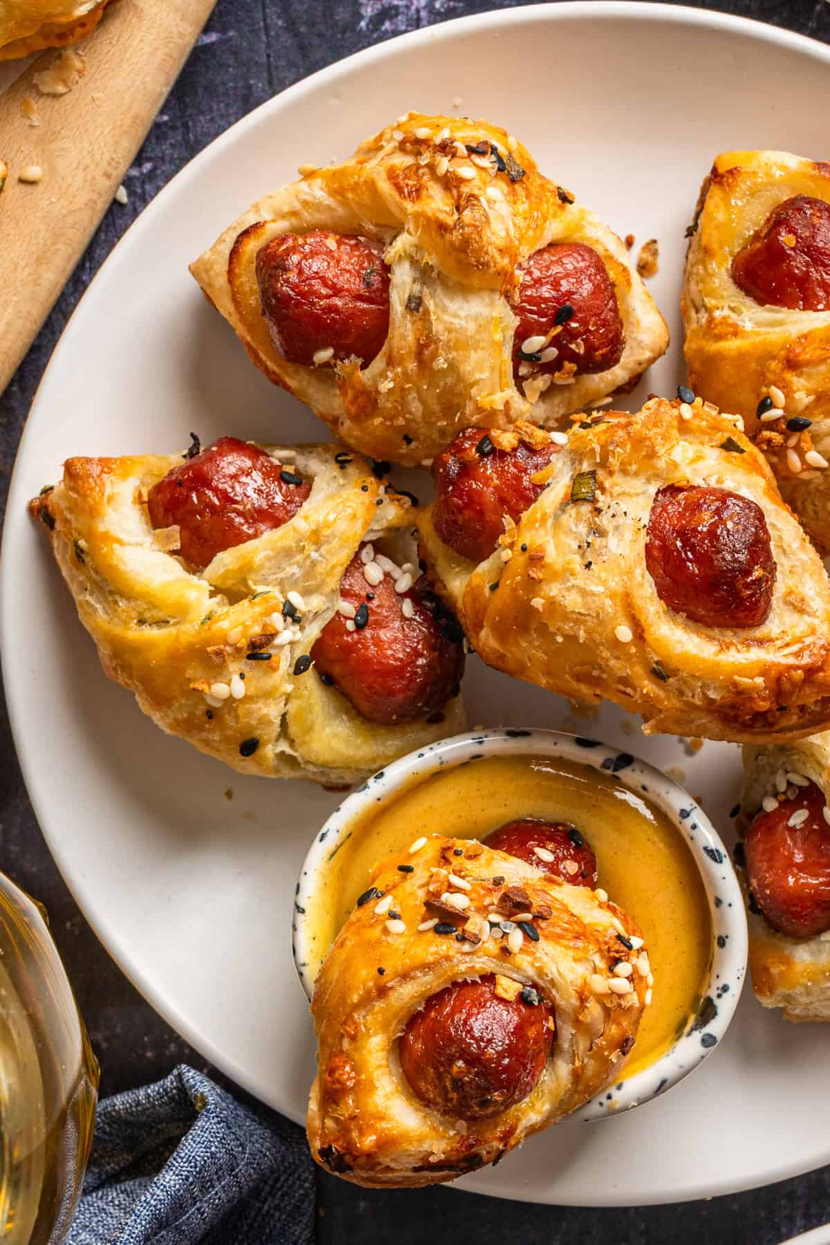 A plate of Pigs in a Blanket - golden-brown pastry-wrapped sausages sprinkled with seasoning, served with a small bowl of dipping sauce.