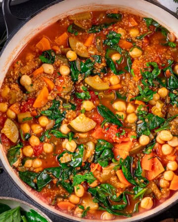 A pot filled with vegetable quinoa soup featuring chickpeas, carrots, zucchini, spinach, tomatoes, and herbs in a rich broth.