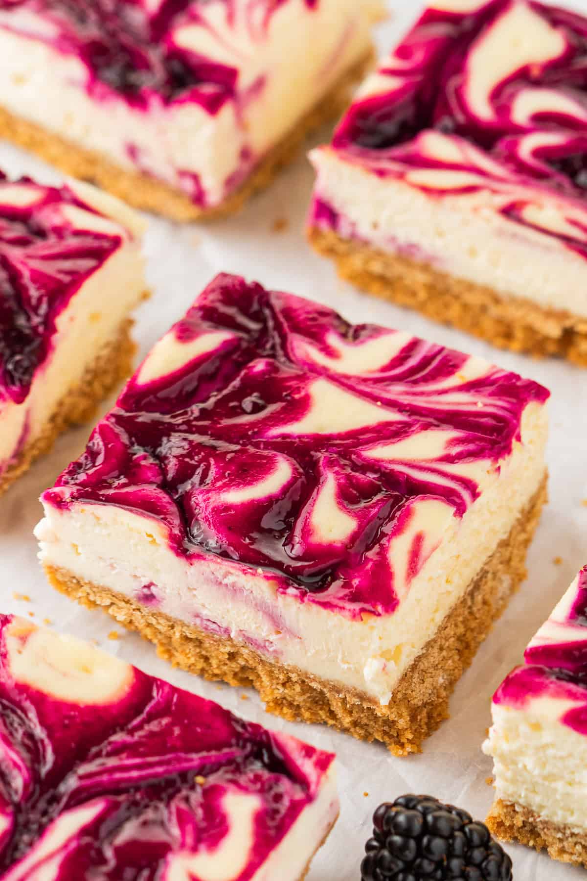 Close-up of blackberry cheesecake bars with a golden crust and swirled berry sauce on top, creating a marbled purple and white pattern.