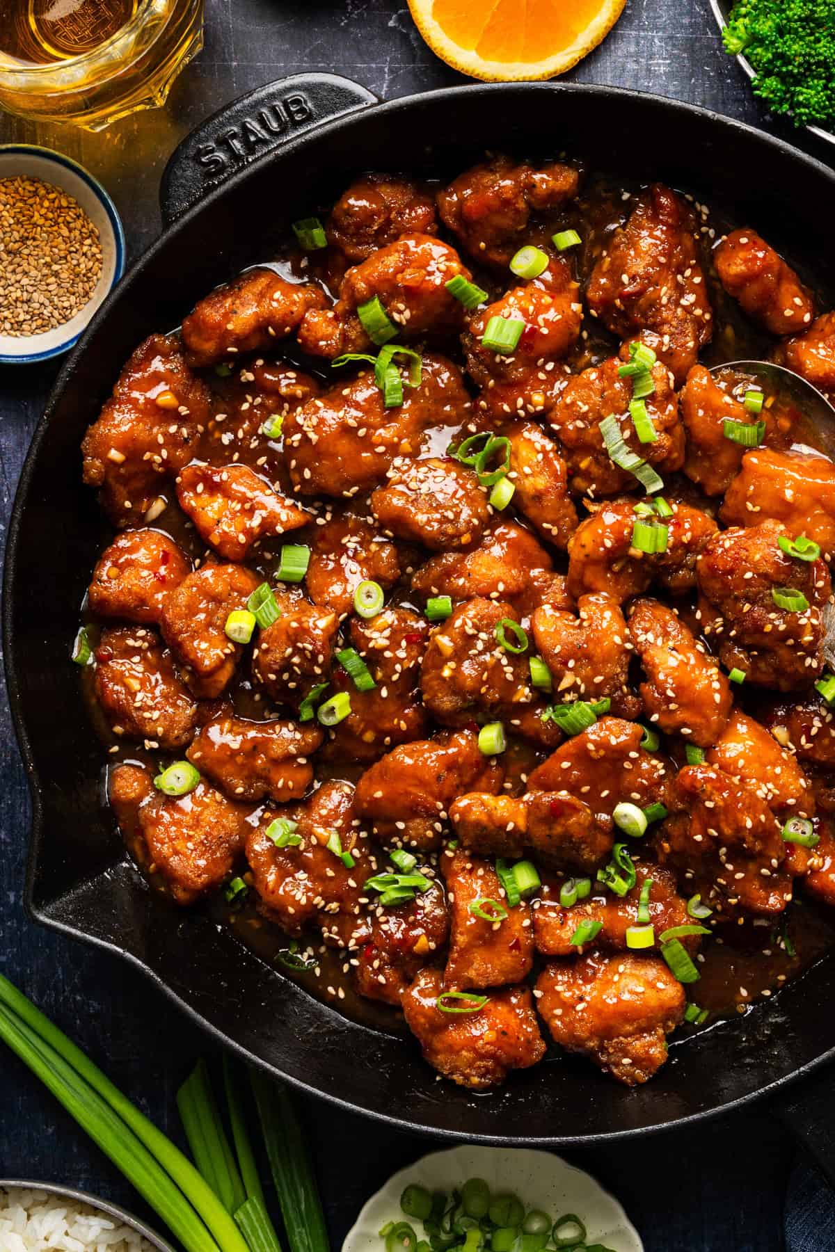 Orange Chicken A skillet filled with glazed orange chicken pieces, garnished with chopped green onions and sesame seeds.