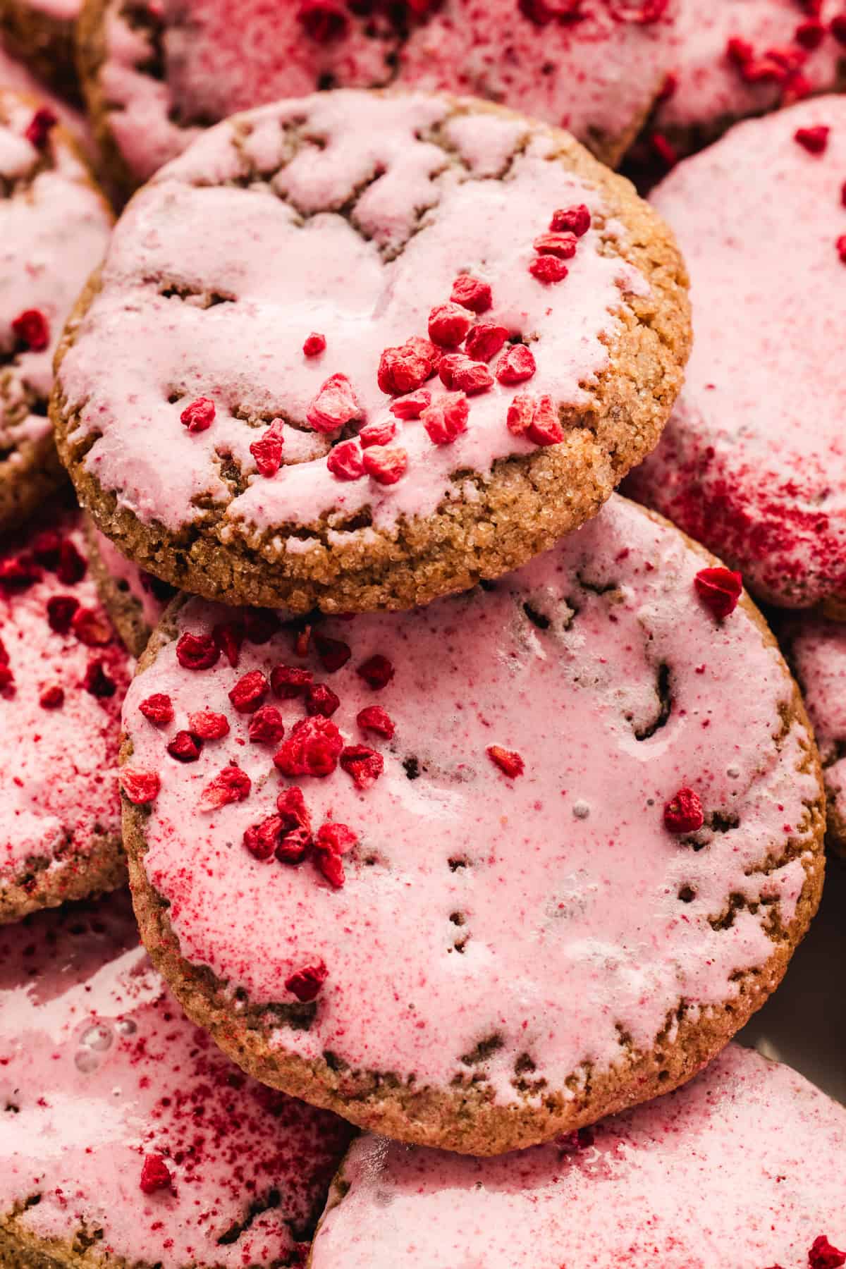 Close-up of raspberry cookies topped with pink icing and sprinkled with small dried raspberries.