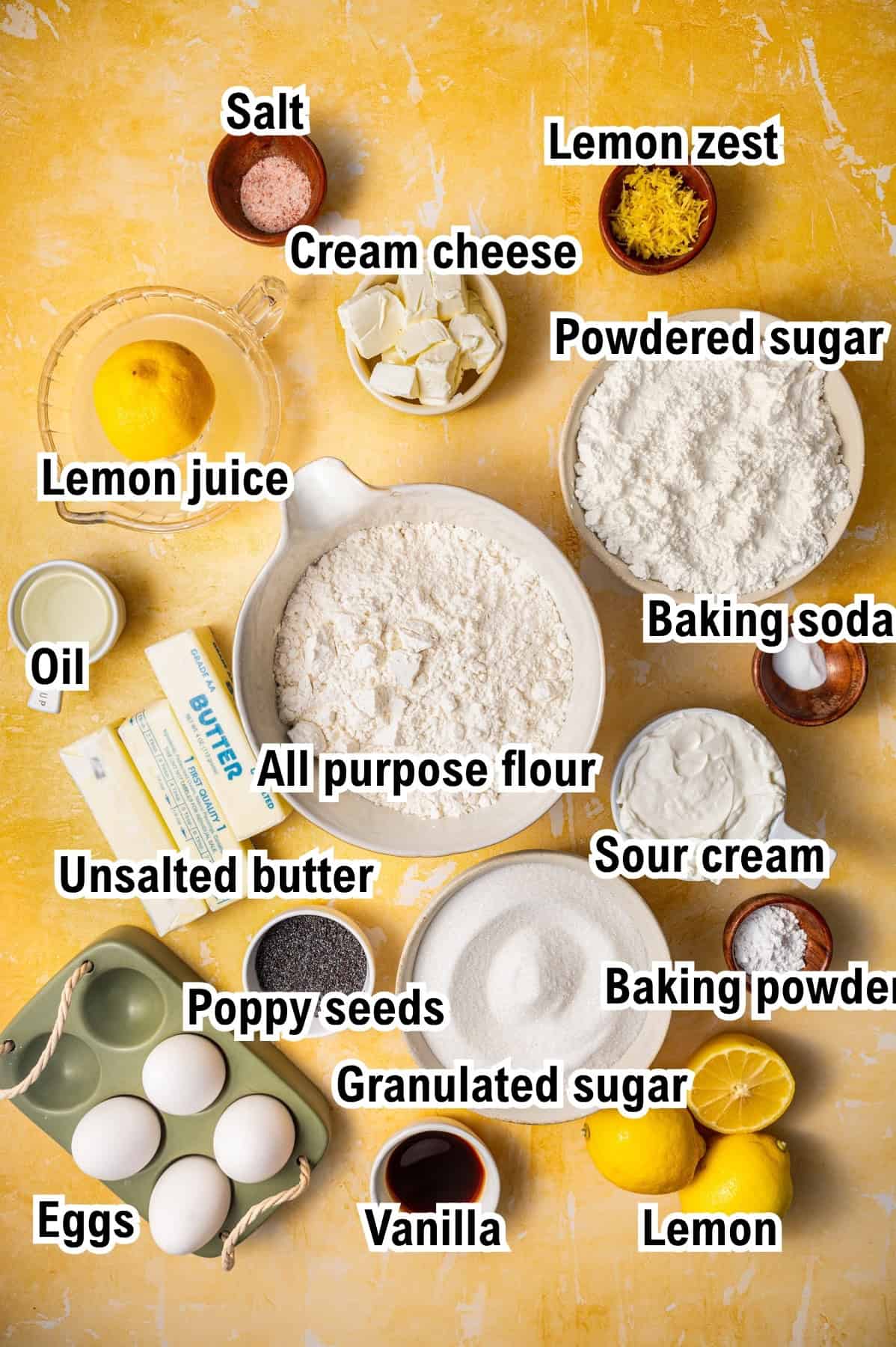 The Ingredients for Lemon Poppy Seed Bundt Cake This photo shows the ingredients for Lemon Bundt Cake: Various baking ingredients in bowls and containers are labeled, including salt, cream cheese, powdered sugar, lemon zest, lemon juice, oil, all-purpose flour, baking soda, unsalted butter, sour cream, baking powder, poppy seeds, granulated sugar, vanilla, eggs, and lemons.