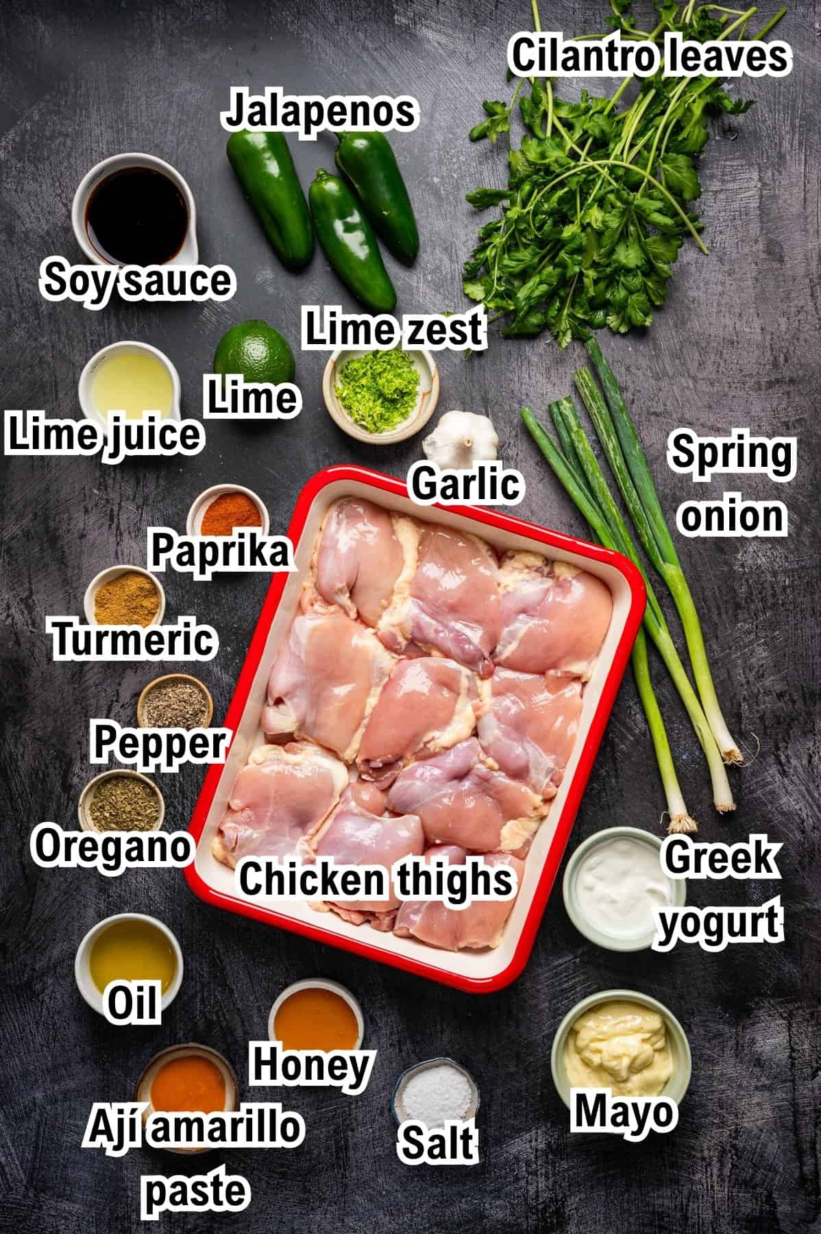 A top-down view of labeled ingredients for a Peruvian Chicken recipe, including chicken thighs, spices, sauces, herbs, lime, jalapenos, garlic, spring onions, Greek yogurt, mayo, oil, honey, and aj&iacute; amarillo paste.