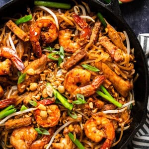 A skillet filled with shrimp, chicken, tofu, bean sprouts, green onions, peanuts, and pad thai noodles, all mixed together in a colorful pad thai dish.