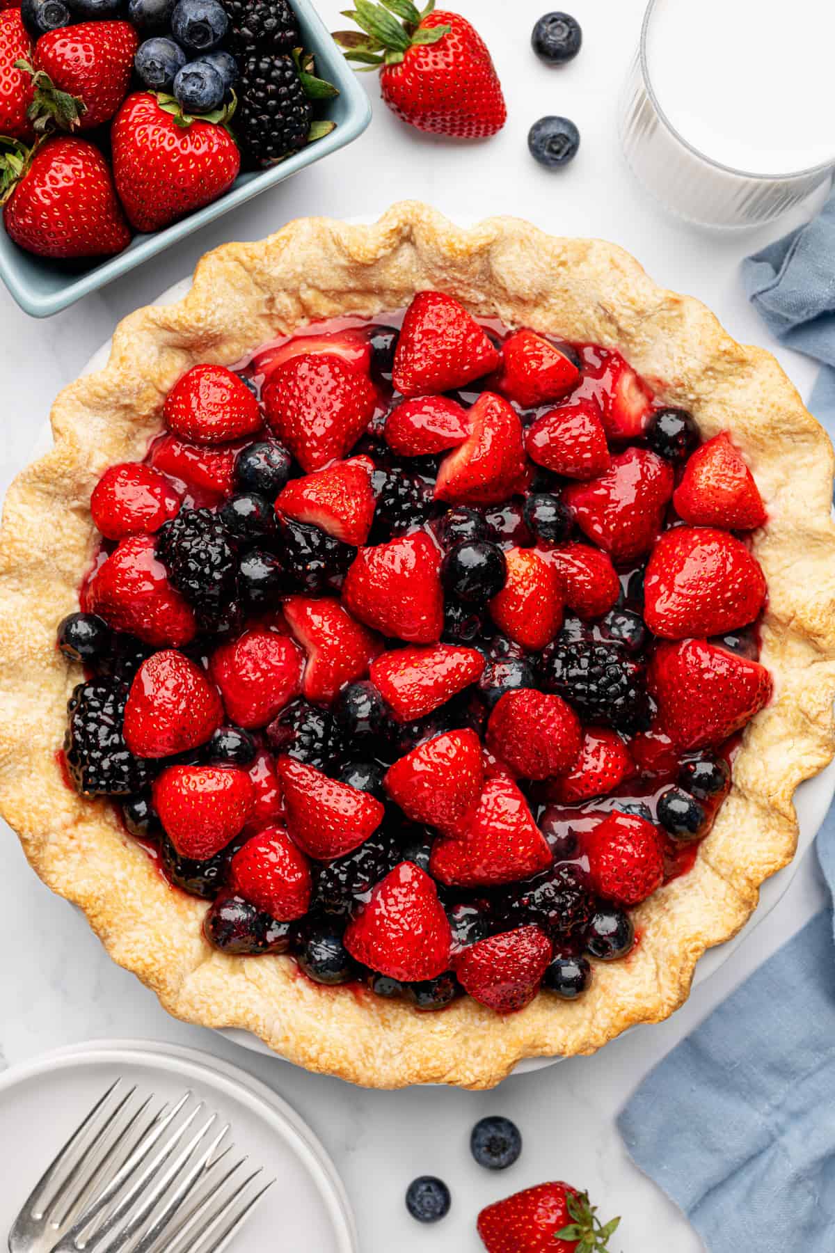 Berry Pie A baked pie filled with glossy strawberries, blackberries, and blueberries sits on a table.