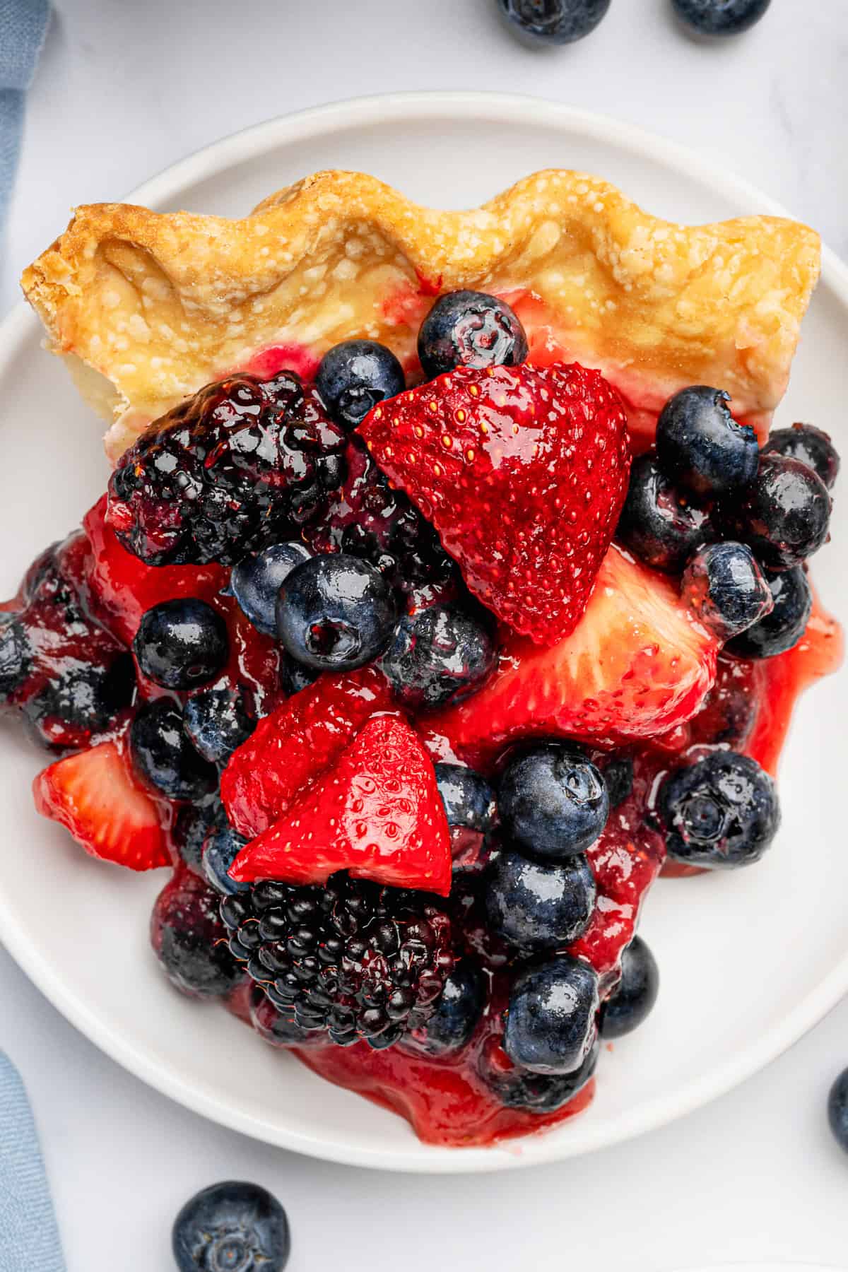 Berry Pie A slice of berry pie topped with fresh blueberries, strawberries, and blackberries, served on a white plate.