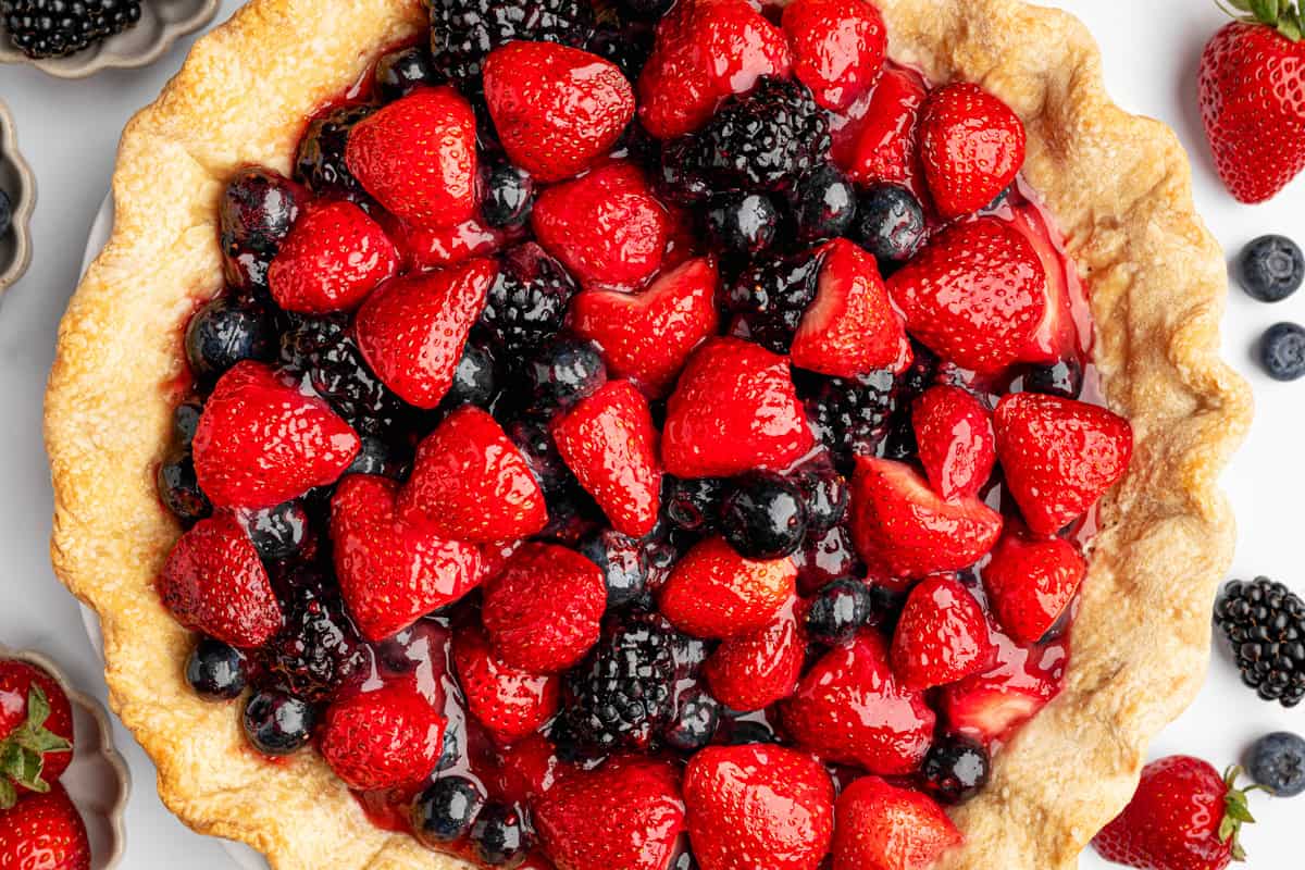 Berry Pie A baked pie filled with fresh strawberries, blackberries, and blueberries, all coated in a glossy glaze.