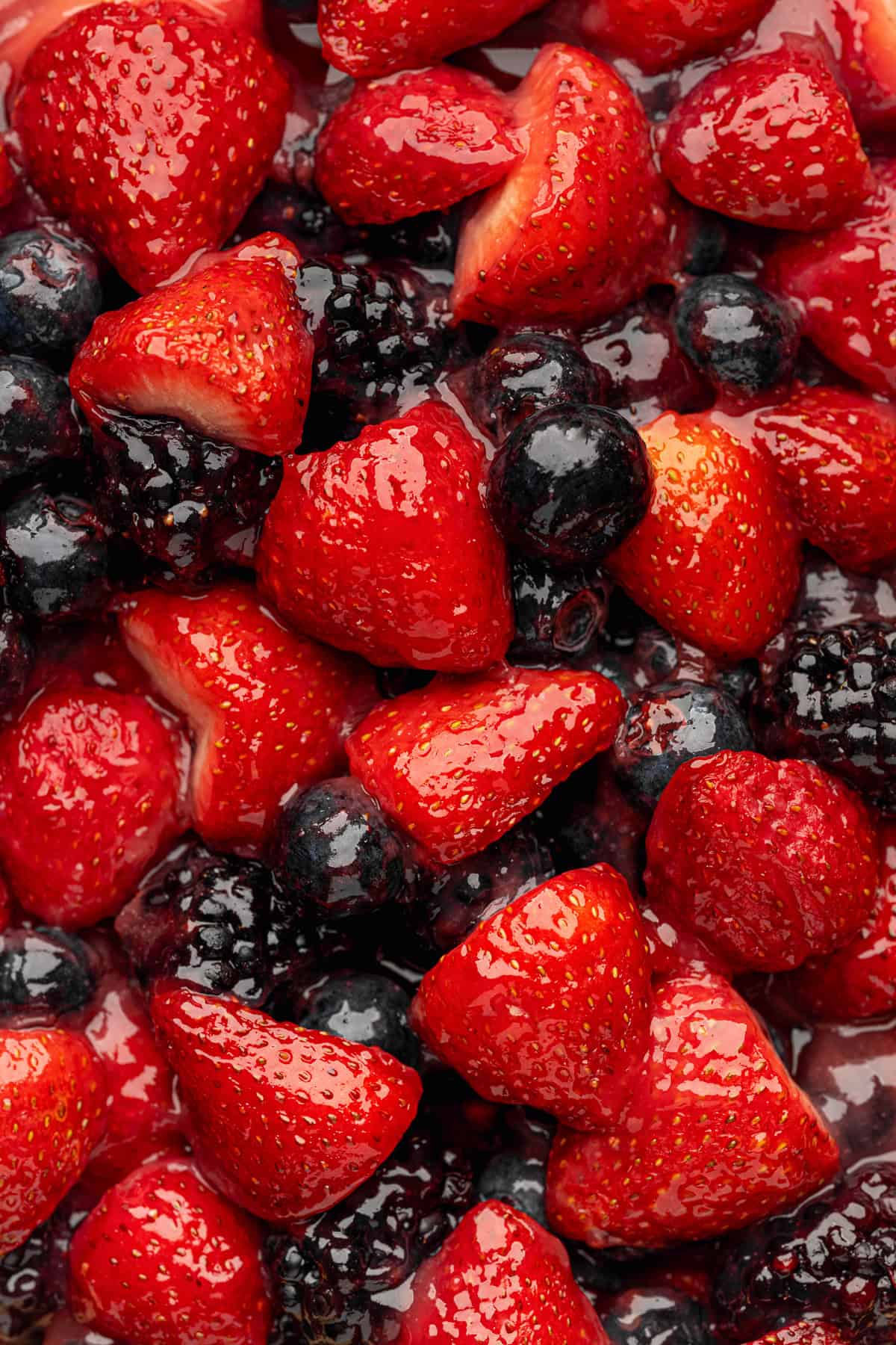 Berry Pie A close-up of glossy, fresh strawberries, blackberries, and blueberries mixed together, showing bright red and deep purple colors with a shiny, juicy appearance.