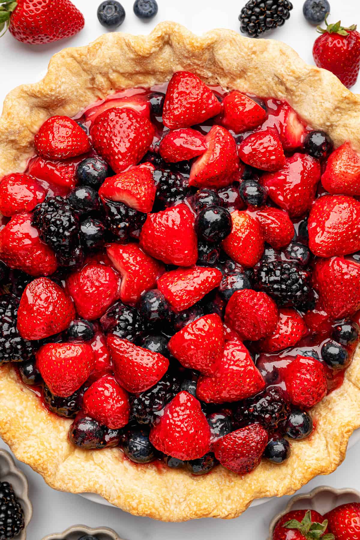 Berry Pie A pie with a golden crust filled with whole strawberries, blueberries, and blackberries in a glossy red glaze.