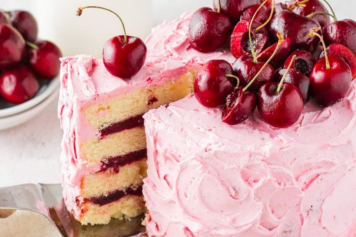 Cherry Layer Cake A sliced cherry layer cake with pink frosting and fresh cherries on top. The inside shows yellow cake layers with cherry filling.