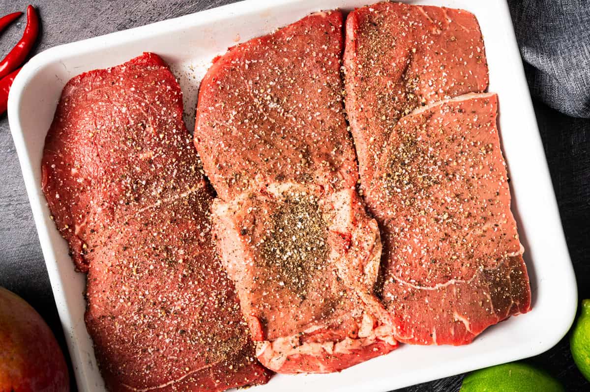 Thai Beef Salad (Step-by-Step Photos) Raw beef steaks are laid out in a white dish, seasoned with cracked black pepper and spices.