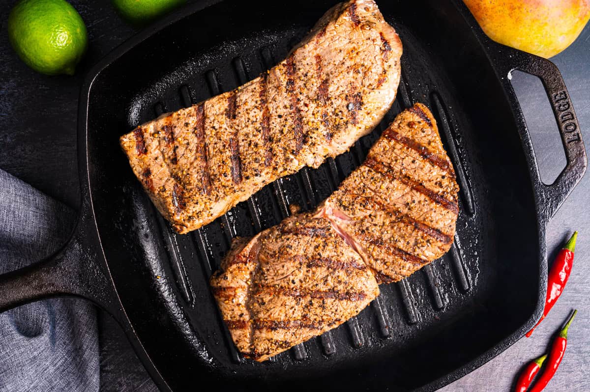 Thai Beef Salad (Step-by-Step Photos) Two seasoned steaks with grill marks cook on a black grill pan.