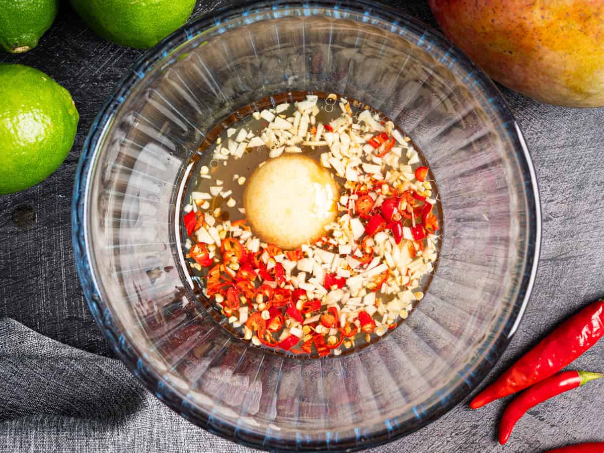 Thai Beef Salad (Step-by-Step Photos) A glass bowl contains chopped red chili, garlic, and a light brown sauce.