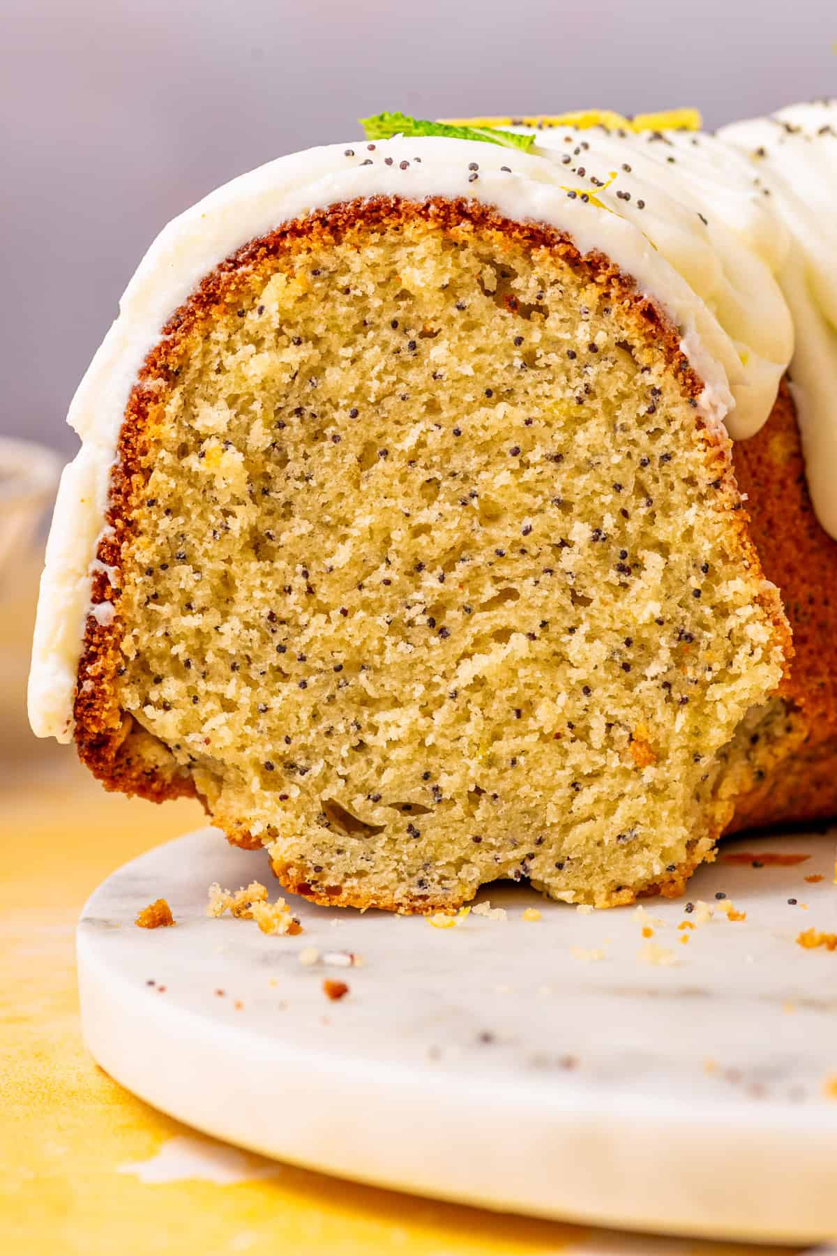 Poppy Seed Lemon Bundt Cake A close-up of a sliced poppy seed bundt cake with white icing on top.