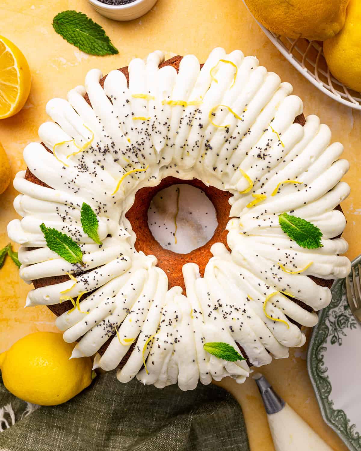 Poppy Seed Lemon Bundt Cake A bundt cake with white icing, topped with lemon zest, mint leaves, and poppy seeds.