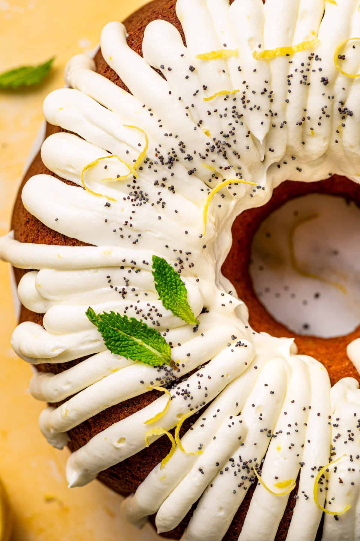 Poppy Seed Lemon Bundt Cake A bundt cake topped with thick white icing, lemon zest, poppy seeds, and fresh mint leaves, shown from above.