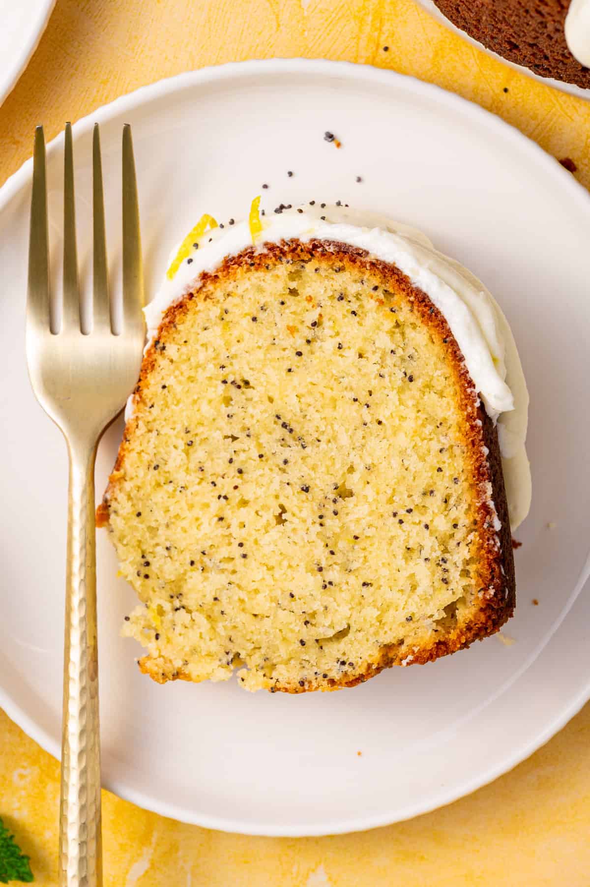 Poppy Seed Lemon Bundt Cake A slice of lemon poppy seed cake with white icing on a white plate.