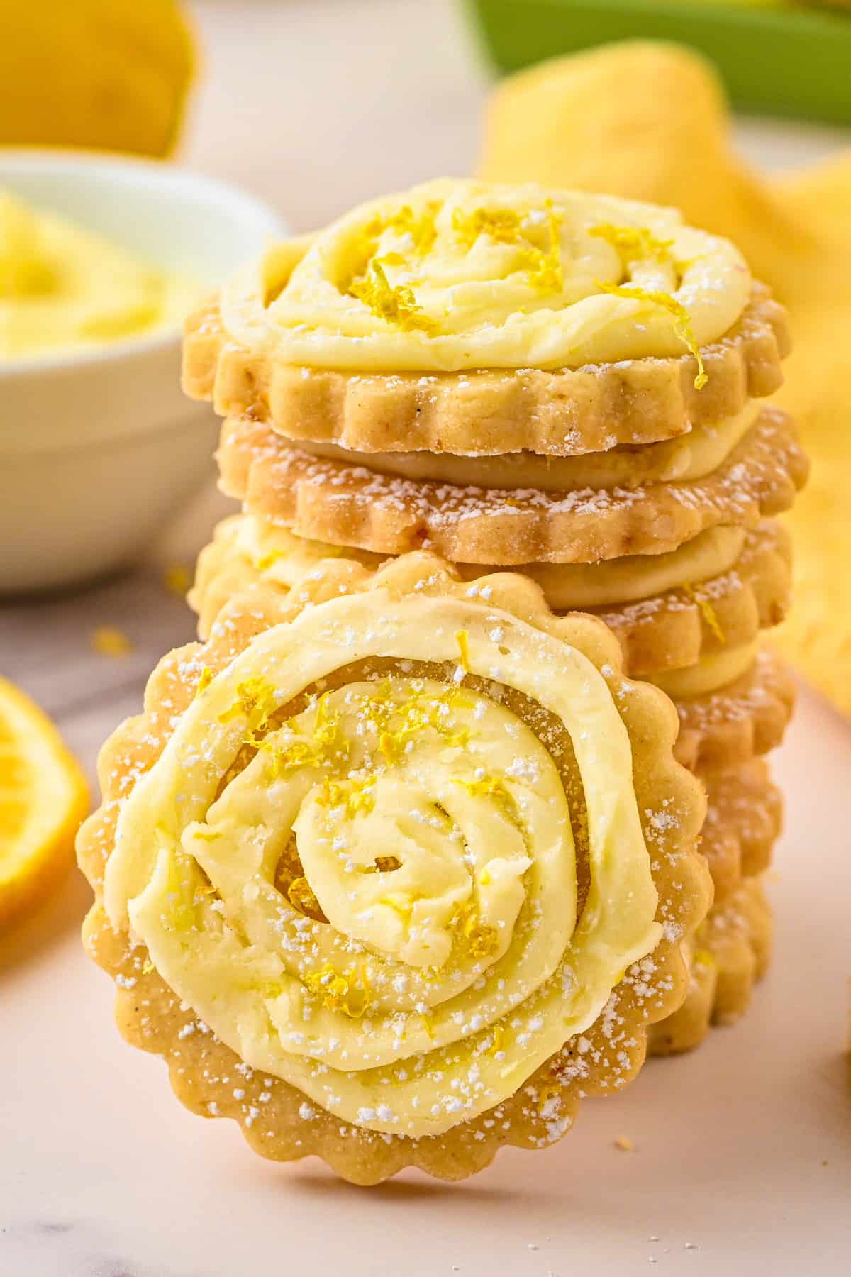 Lemon Shortbread Cookies A stack of round lemon cookies with creamy lemon frosting and zest on top, dusted with powdered sugar.