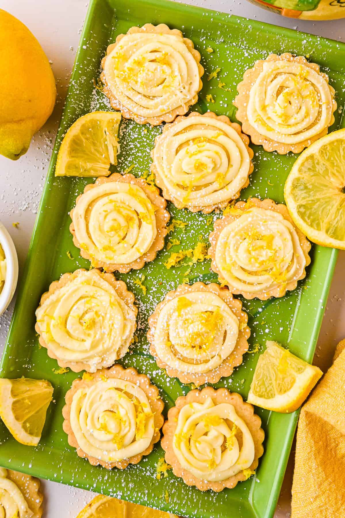 Lemon Shortbread Cookies A green tray holds lemon shortbread cookies topped with swirled lemon frosting, lemon zest, and powdered sugar.